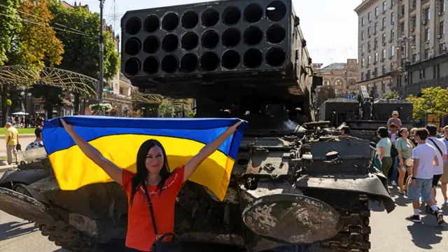 A woman poses with the Ukrainian flag in Kyiv at an exhibition of destroyed Russian military equipment