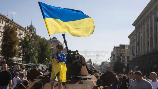 A boy waves a national flag atop of armoured personal carrier at an exhibition of destroyed Russian military vehicles and weapons in Kyiv