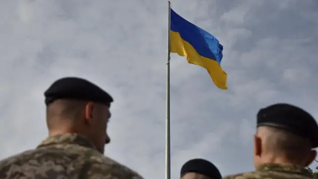 The flag is seen from a distance with servicemen in the foreground