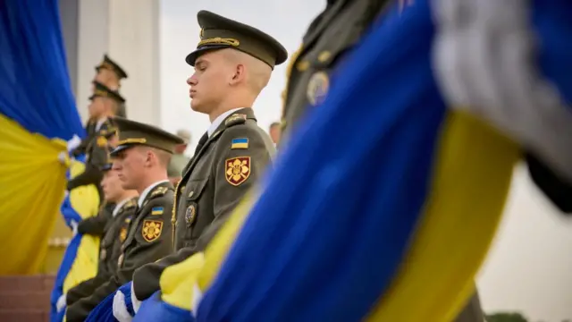 Ukrainian servicemen pass a large flag from person to person