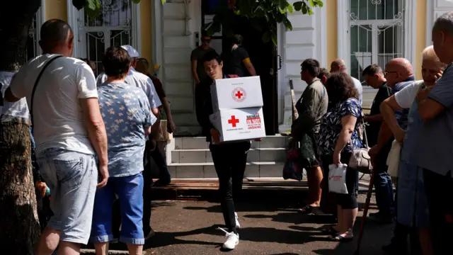 People wait to collect humanitarian aid at a Red Cross distribution point in Mykolaiv