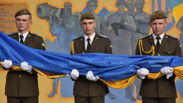 Ukrainian servicemen pass a large flag from person to person