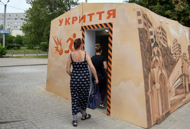 Locals go inside of a small bomb shelter installed near one of the bus stops for public transport passengers in Kharkiv, Ukraine, 20 August 2022