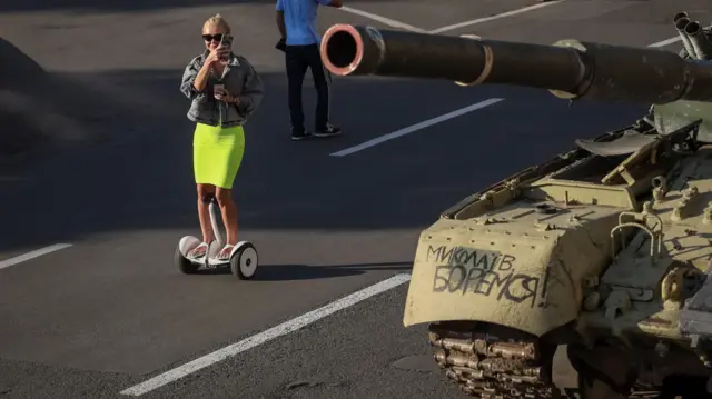 A woman rides on a scooter near a destroyed Russian tank on Kyiv's main street Khreshchatyk as part of the celebration of the Independence Day of Ukraine