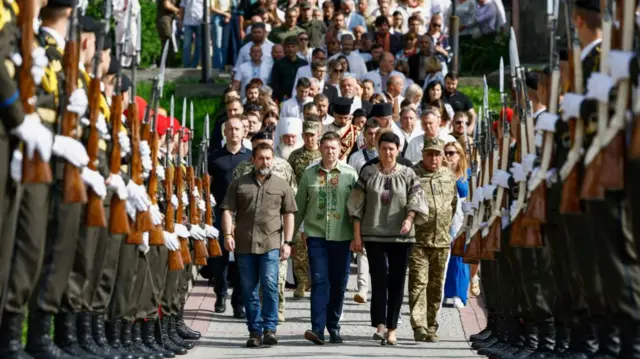 People walk alongside a military guard at a ceremony at the graves of fallen soldiers in Lychakiv cemetery