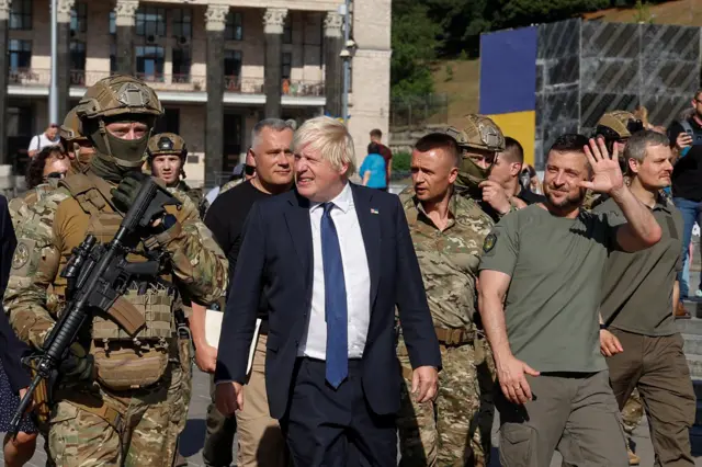 Johnson and Zelensky walk down across a square in Kyiv, Zelensky waves as both are flanked by a throng of military personnel