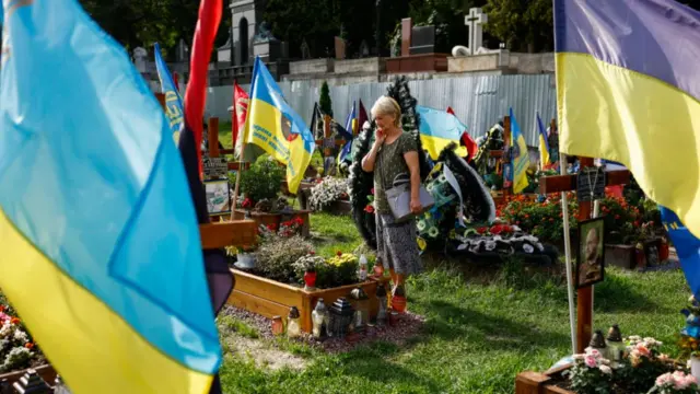 A woman stands among graves and flags at a ceremony for fallen soldiers in Lychakiv cemetery