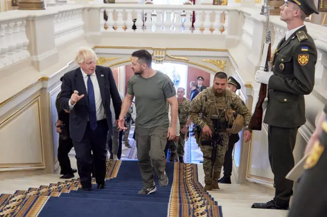 Johnson and Zelensky walk up some stairs together, flanked by military personnel