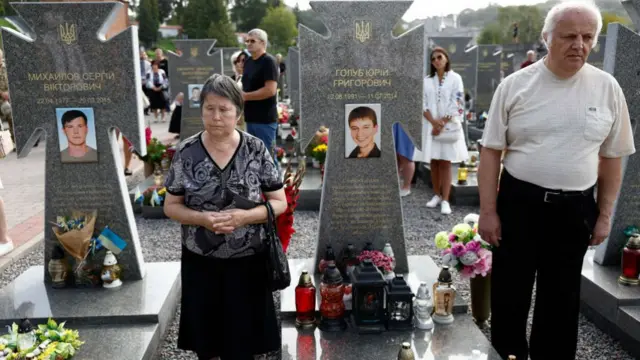 A woman and man stand among graves at a ceremony for fallen soldiers in Lychakiv cemetery