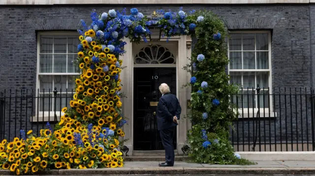 Boris Johnson outside 10 Downing Street, looking at a huge display of sunflowers and blue flowers around the door to mark Ukraine's Independence Day