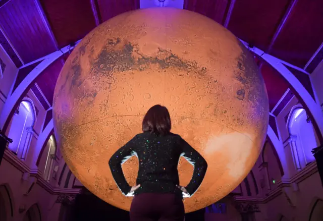 A woman looks up at a Luke Jerram's art installation representing Mars in Dorchester, UK, in March 2022