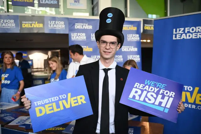 Man in top hat showing Truss and Sunak signs