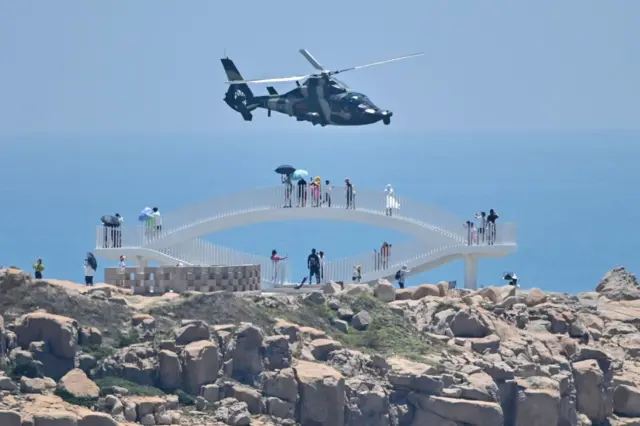 Tourists look on as a Chinese military helicopter flies past Pingtan island