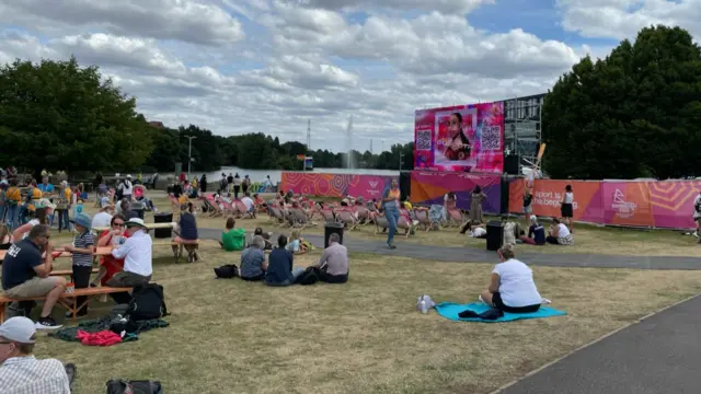 Fans sit on the grass in front of a big screen