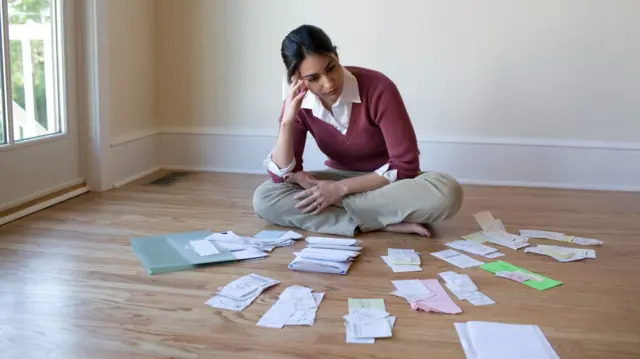 woman sat on floor looking stressed, surrounded by receipts