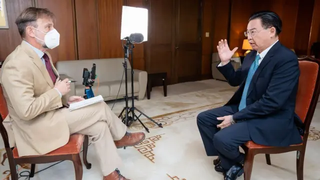 The BBC's Rupert Wingfield-Hayes, in a cream suit, sits opposite and interviews Taiwan Foreign Minister Joseph Wu