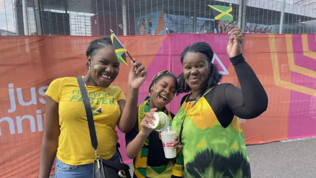 Ebony, Olivia and Kay cheering and waving Jamaica flags