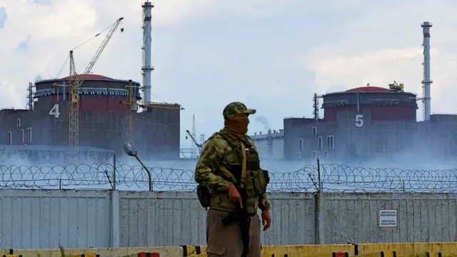 A serviceman with a Russian flag on his uniform stands guard near the Zaporizhzhia nuclear power plant