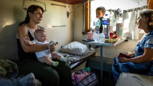 A woman and her two children sitting in a train travelling from the Donetsk region to Dnipto