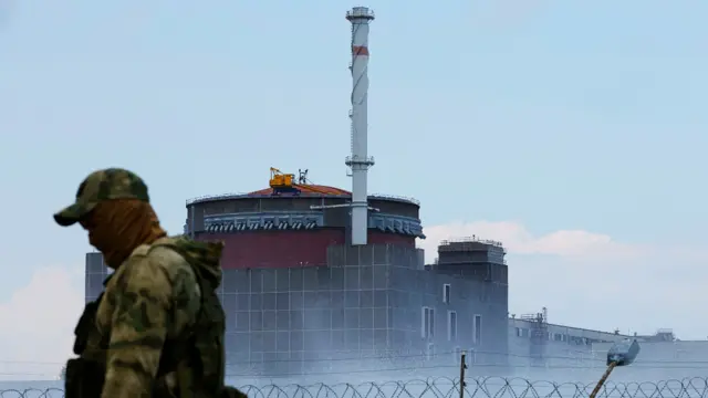 A serviceman with a Russian flag on his uniform stands guard near the Zaporizhzhia nuclear power plant