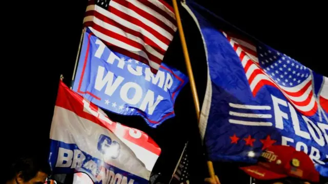 Supporters of former U.S. President Donald Trump wave flags as they gather outside his Mar-a-Lago home after Trump said that FBI agents raided it