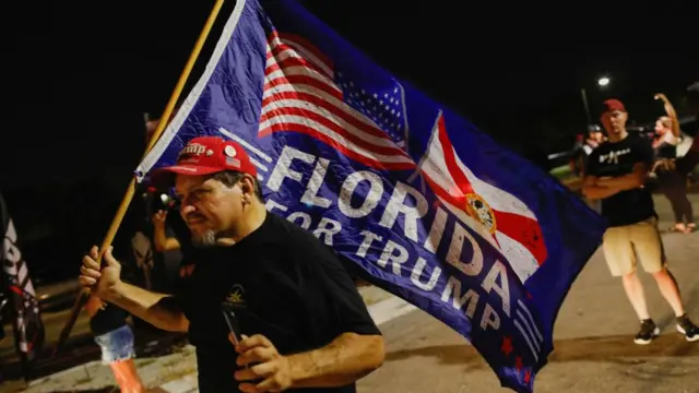 A supporter of former U.S. President Donald Trump waves a flag as he and others gather outside his Mar-a-Lago home after Trump said that FBI agents raided it