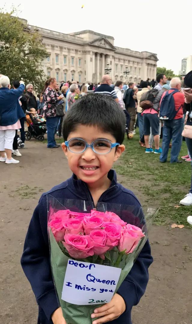 Five-year-old Zak holds a bunch of flowers outside Buckingham Palace