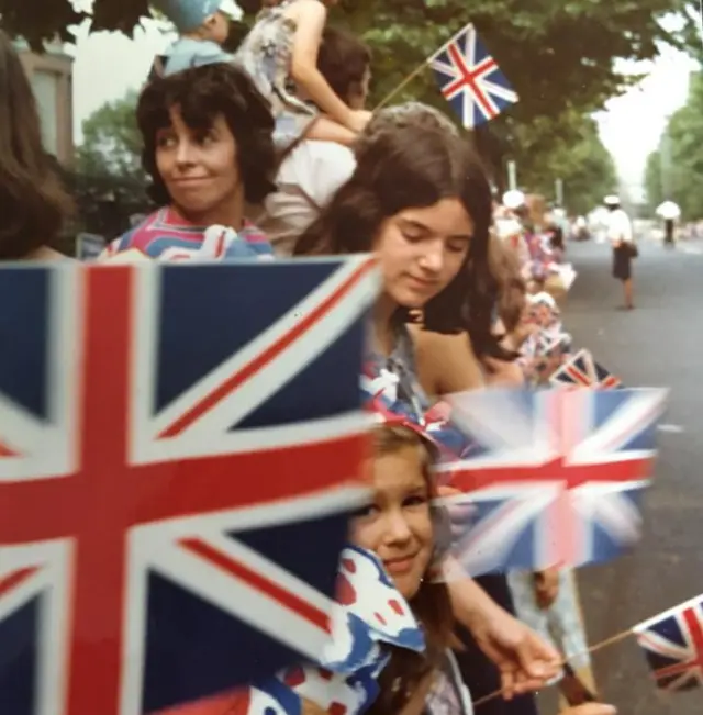 Cathy, between the flags, watching and waiting for The Queen