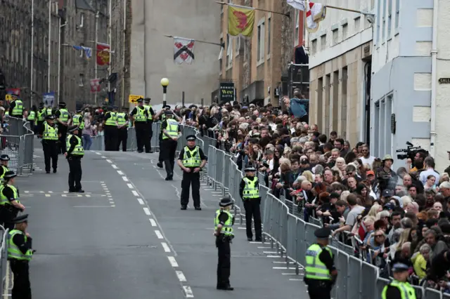 People wait at The Royal Mile for the arrival of the hearse