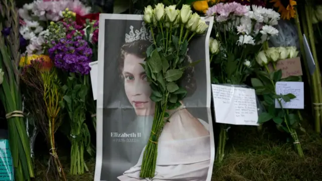 A newspaper featuring the Queen's portrait is laid alongside a bunch of flowers