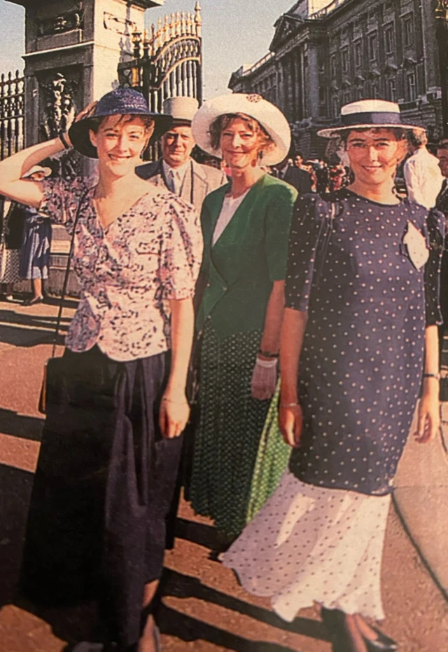 Elizabeth and her sister stand outside of Buckingham Palace after being presented to the Queen, they wear hats, lace gloves and long dresses