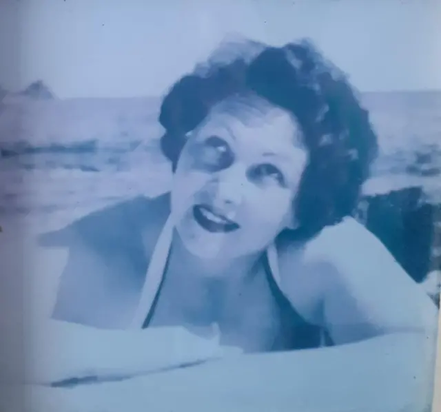 Tamsin's mother poses for a photograph on the beach in an old black and white photo with her hair in tight curls