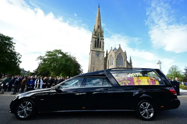 Members of the public pay their respects as the hearse carrying the coffin of Queen Elizabeth II, draped in the Royal Standard for Scotland, is driven through Ballater, on 11 September 2022