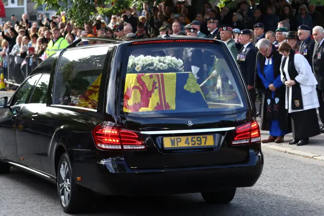 Cortege passes through Ballater, clergy can be seen bowing their heads as a line of people watch on