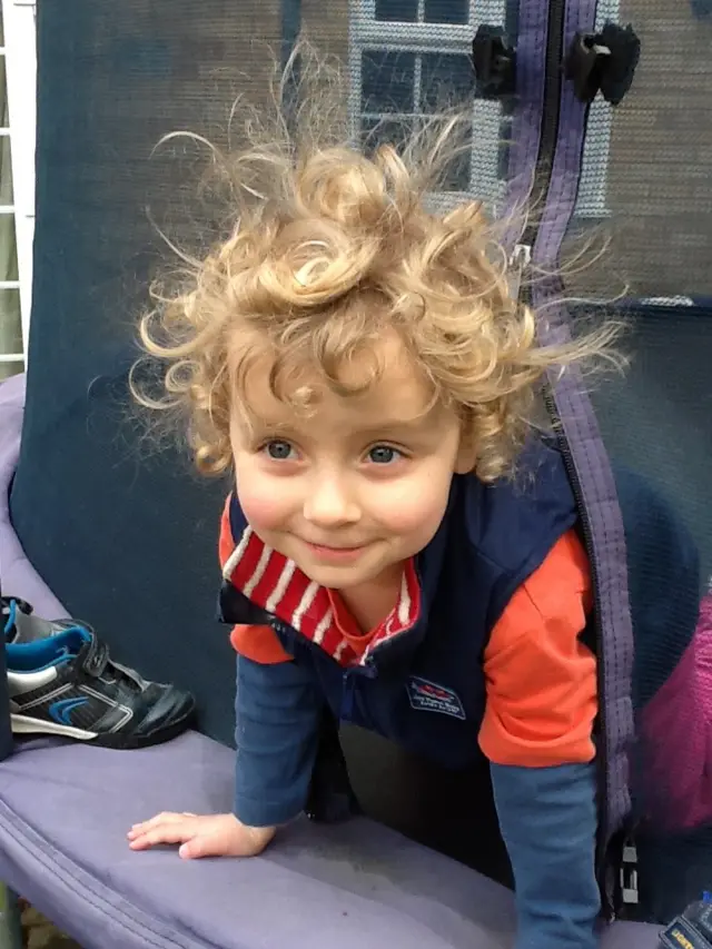 A little girl aged three with blonde curls smiles as she leaves her trampoline