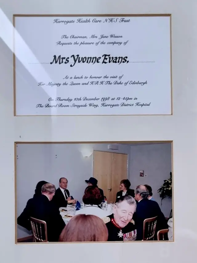 A framed photograph given to Yvonne of the Queen and Prince Phillip having lunch with staff at Harrogate Hospital with her invitation framed also above the photo