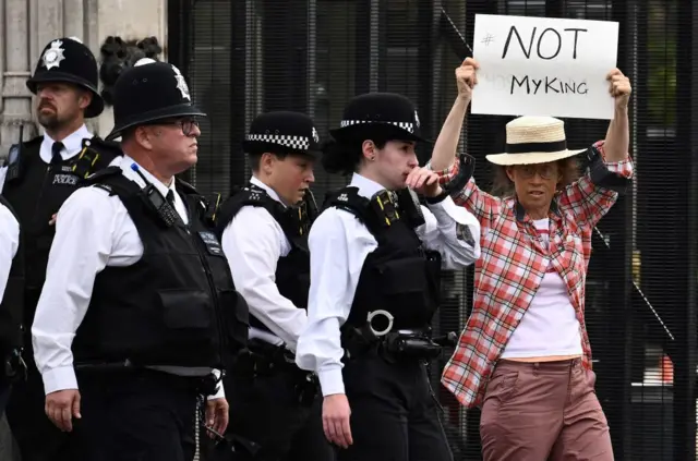 A protester with the sign "not my King" moved on by police