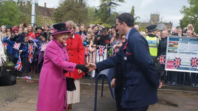 Keith Webber meeting the Queen at Sherborne station the Queen is wearing a bright pink coat and matching hat as she shakes his hand and people gather behind them with union jack flags