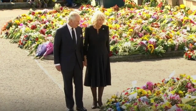 King Charles III and his Queen Consort Camilla view flowers left outside the castle