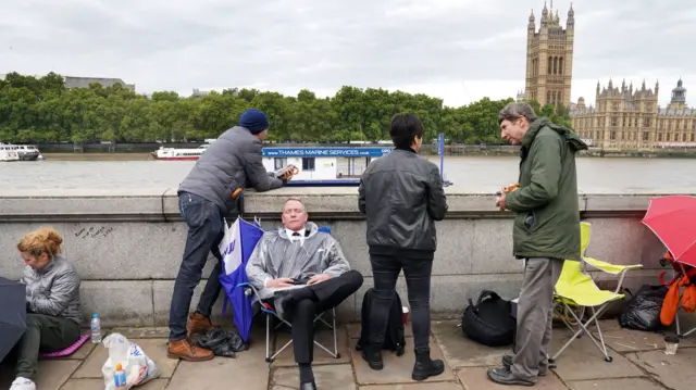 Man sitting in foldable chair in Queue