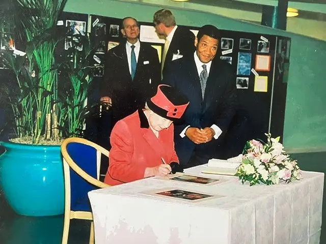 Hugh Howe standing next to the Queen as she signs a picture