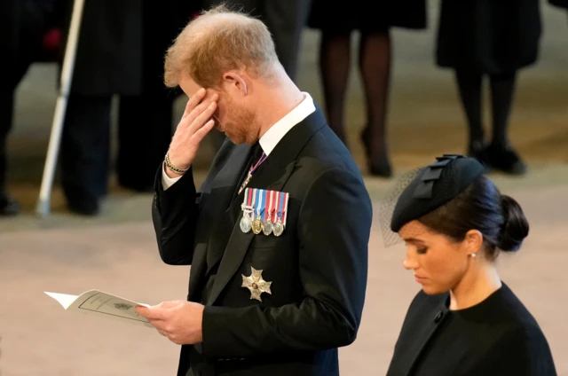 Prince Harry with his hand over his eyes, next to Meghan, as Westminster Hall service begins