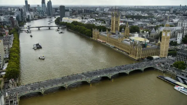 Aerial shot of crowds of people crossing Westminster Bridge by the Palace of Westminster