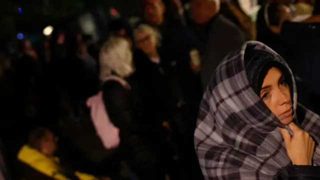 A woman, with her hood up, wraps herself in a blanket in the queue to see the Queen's coffin