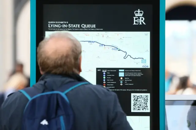 A man at Paddington Station reads a sign advising people of the length of the queue