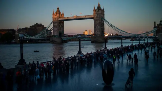 People queue on The Queen's Walk by the Tower Bridge