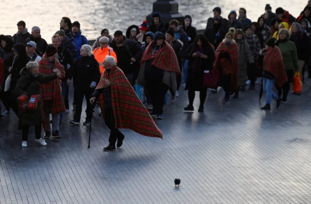 People queue with blankets draped on shoulders