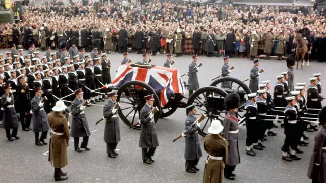 A photo from 1965 shows the State Gun Carriage, pulled by sailors, carrying the coffin of Winston Churchill through Trafalgar Square as crowds watch.