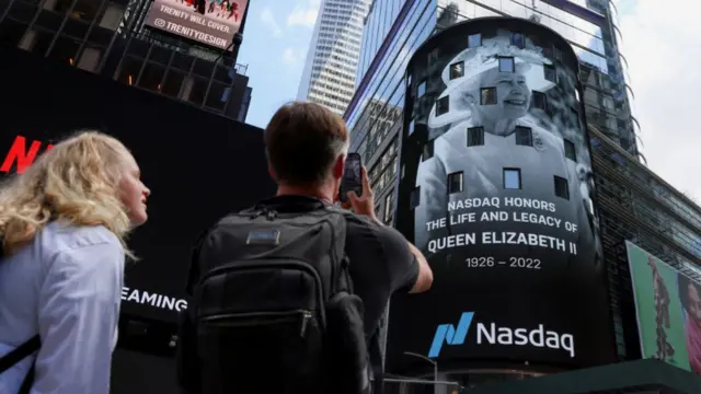 People snap photos of a screen showing the Queen in New York