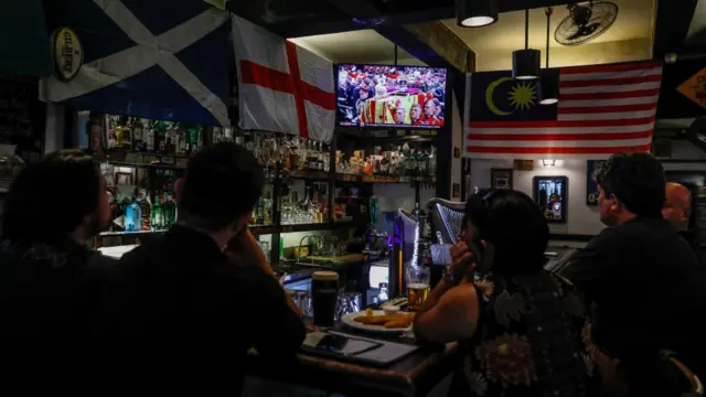 People watch a live TV broadcast of the State Funeral Procession of Queen Elizabeth II in London, Britain, inside a bar at Kuala Lumpur, Malaysia